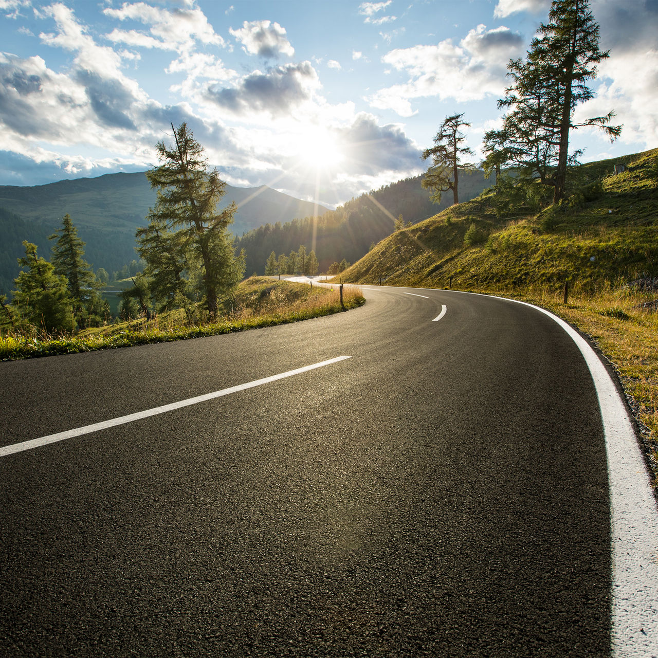 Eine gewundene Straße durch eine idyllische Berglandschaft bei Sonnenaufgang.