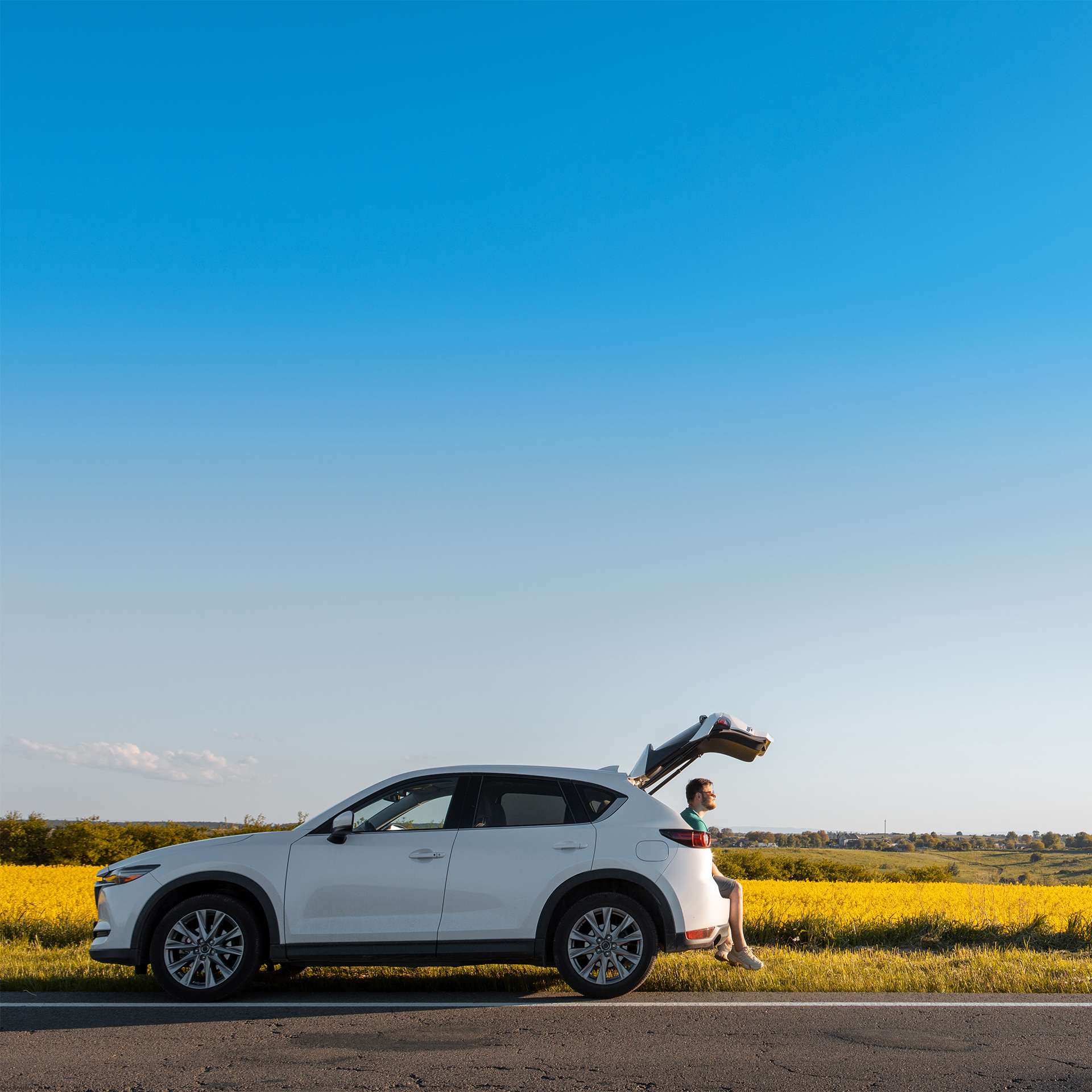 Ein weißer SUV steht am Straßenrand vor einem leuchtend gelben Feld und klarem Himmel.