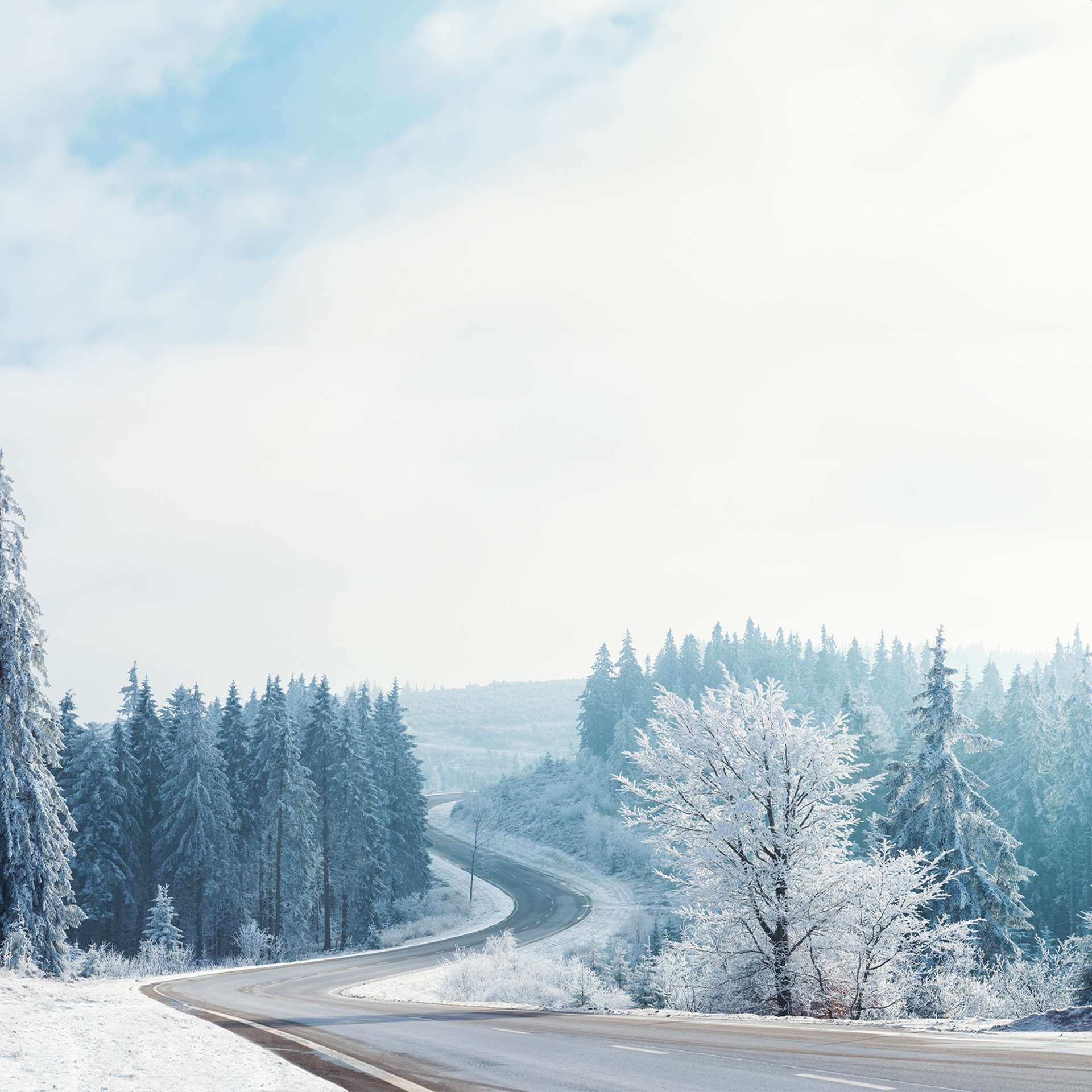 Eine kurvige Landstraße schlängelt sich durch eine verschneite und frostige Winterlandschaft.