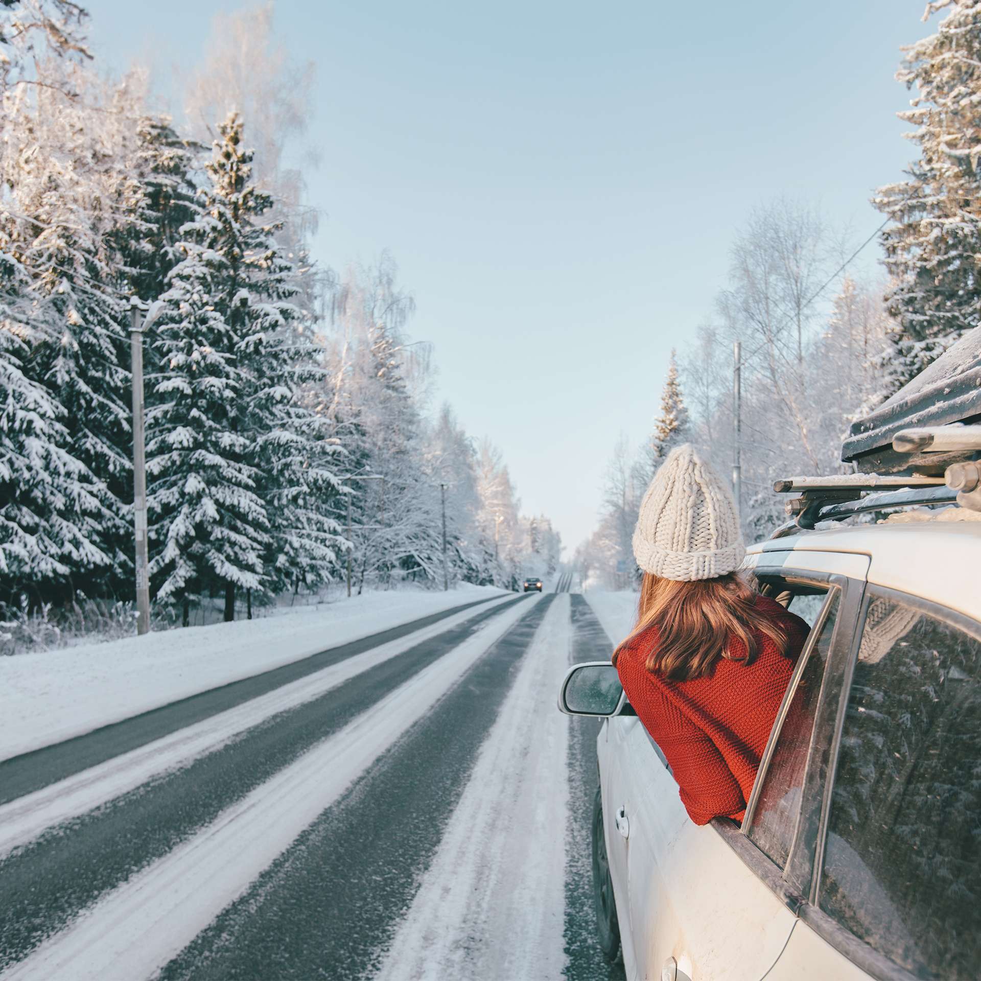 Eine Person schaut aus dem Fenster eines Autos, das auf einer schneebedeckten Straße fährt.