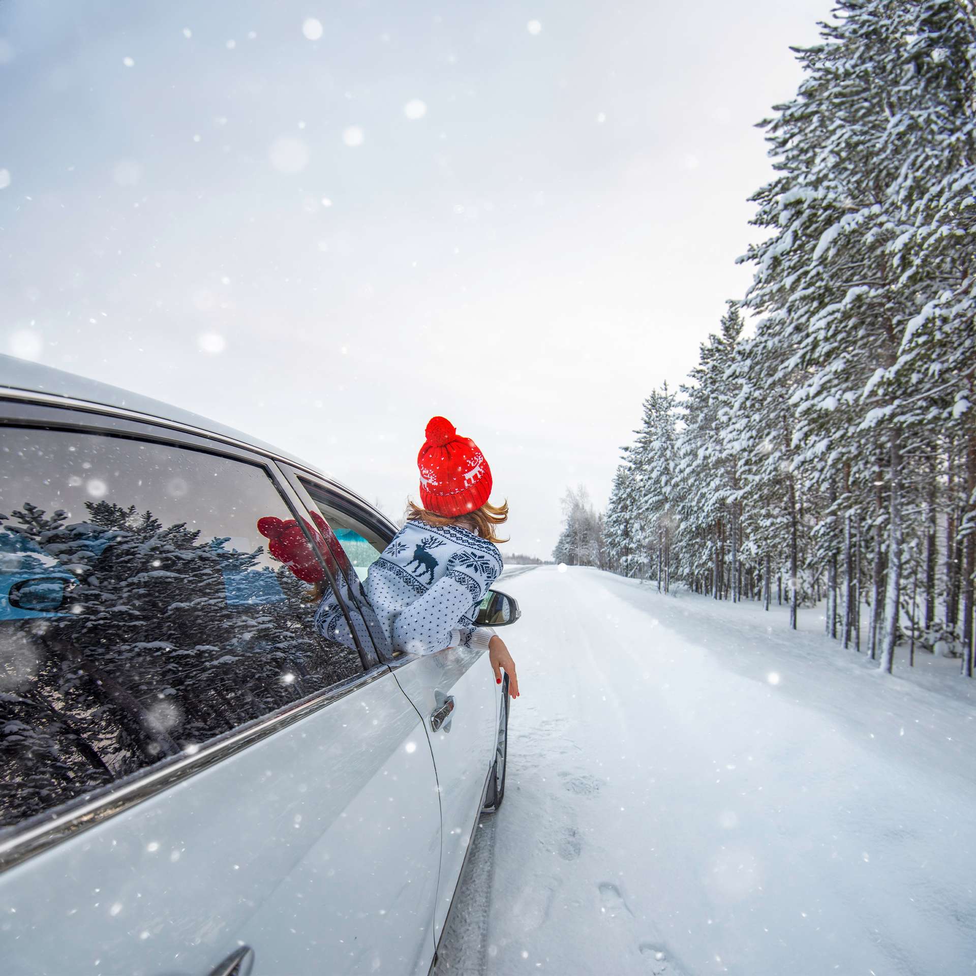 Eine Person lehnt aus einem Autofenster und genießt den Schneefall entlang einer schneebedeckten Straße.