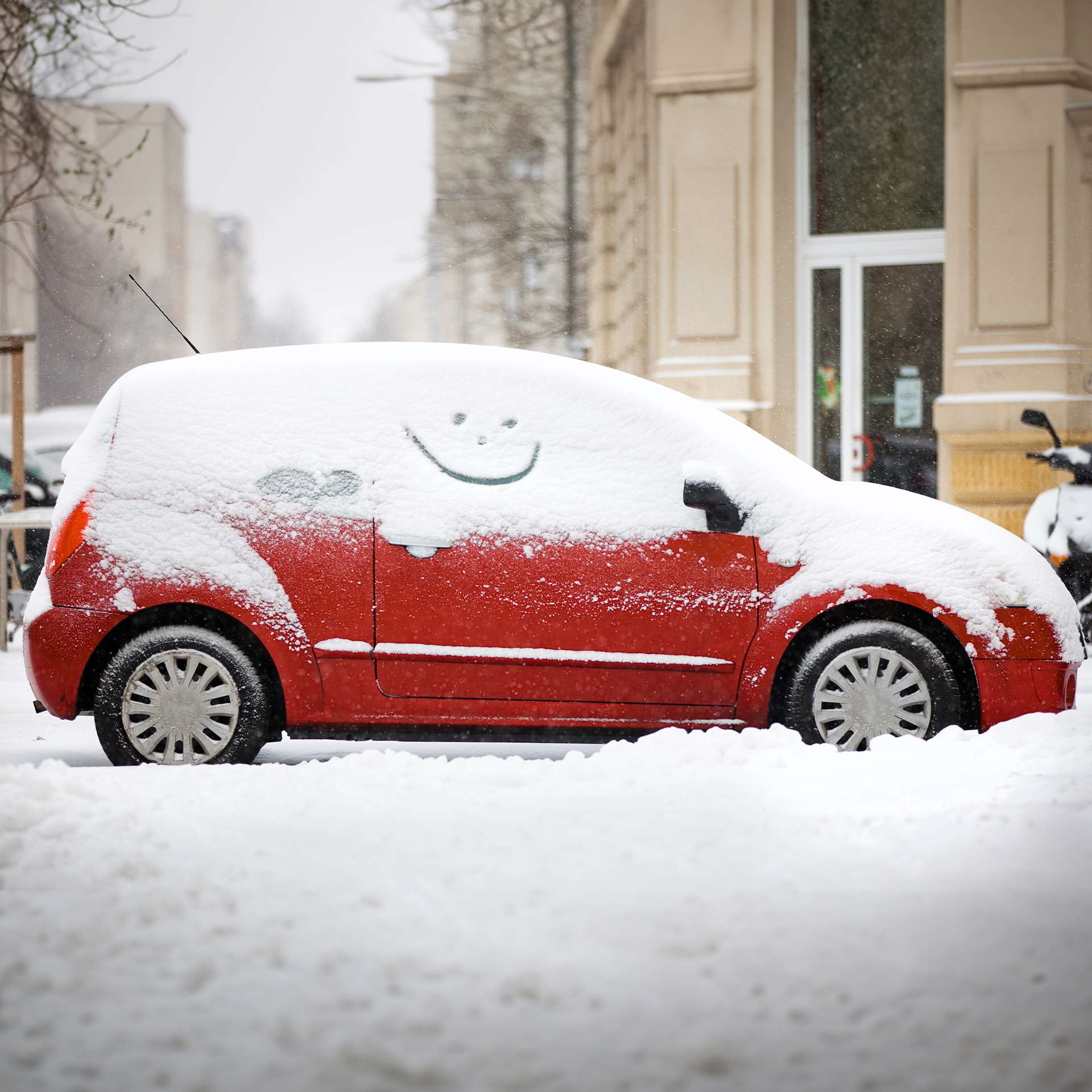 Ein rotes Auto, bedeckt mit Schnee, in einer Stadt mit einem aufgemalten Lächeln.