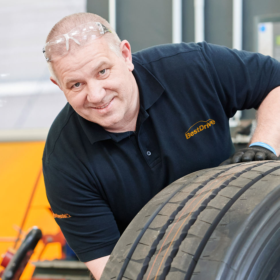 BestDrive Mitarbeiter rollt einen Reifen mit den Händen durch die Werkstatt.