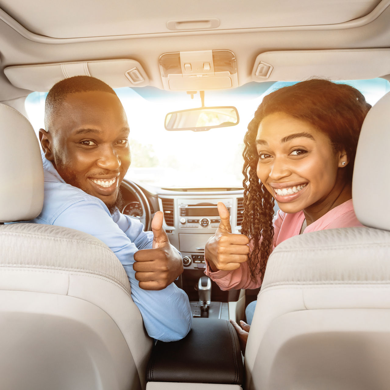 Happy black couple sitting in auto gesturing thumbs up