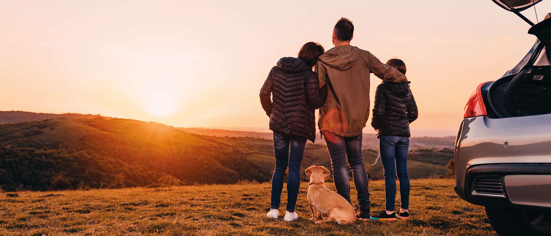 Family with dog embracing at hill and looking at sunset